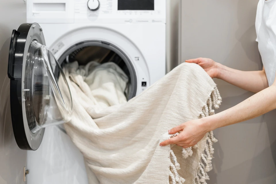 Intérieur domestique moderne avec une femme chargeant du linge blanc dans une machine à laver frontale
