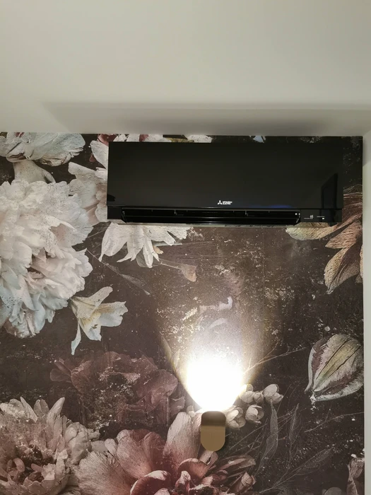 Intérieur résidentiel avec climatiseur mural blanc Mitsubishi installé au-dessus de tableaux encadrés sur mur blanc